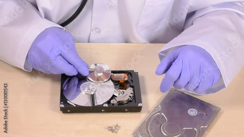 Person in purple rubber gloves and white coat checks hard disk drive with stethoscope, top part and screws lay on table, concept of checking hdd's wellbeing, data security. Close up, 4K Ultra HD.