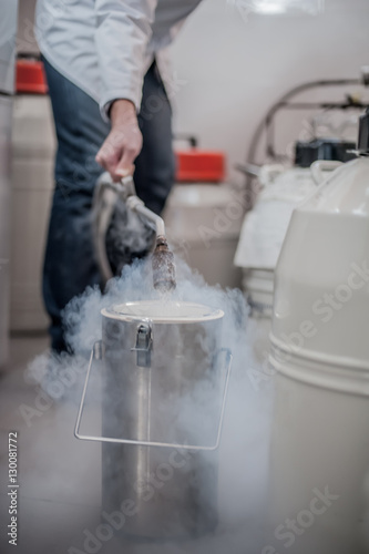 Liquid nitrogen technician fills cryogenic container photo