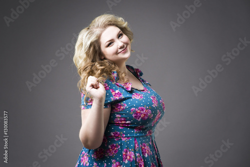 Young beautiful blonde plus size model in dres, xxl woman portrait on gray studio background