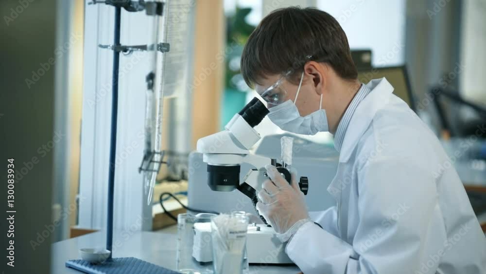 Scientist looking through a microscope in a laboratory Scientist looking through a microscope in a laboratory