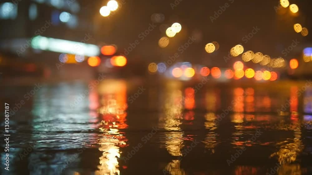 Colorful traffic lights bokeh circles reflecting in water on night city street with small raindrops. Slow motion video