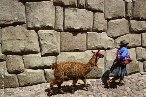 Woman with llama walking along the Inca wall at Hathunrumiyoq Street, Las Piedras del los 12 Angulos (Stone of 12 angles), Cuzco, Peru photo