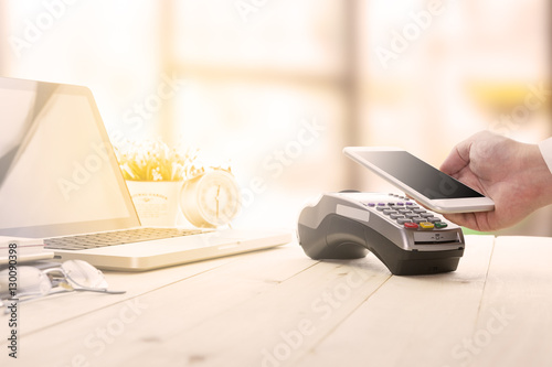 Mobile payments concept with EDC machine or credit card terminal with computer laptop and glasses. Warm toning effect.