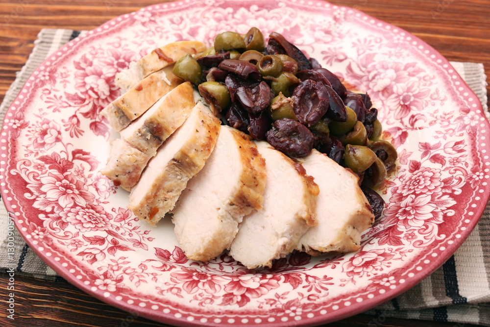 Chicken breasts braised with olives on plate on woden table