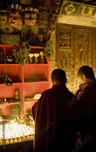 Monks light butter lamps on an auspicious night, watched by two fearsome masks, Boudha stupa, Bodhnath, Kathmandu, Nepal. photo