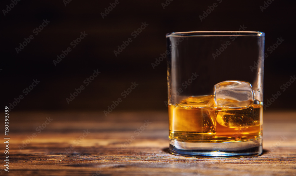 Glass of whiskey with ice cubes served on wood