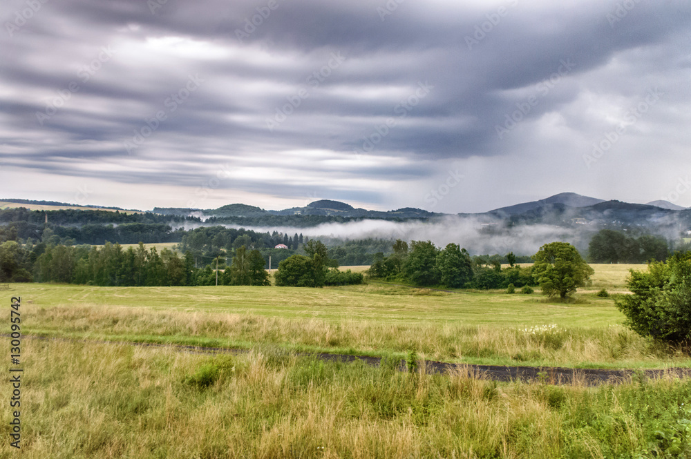 A wide expanse of green fields with hills in the background