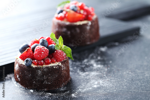 Sweet chocolate cakes with berries on black wooden table
