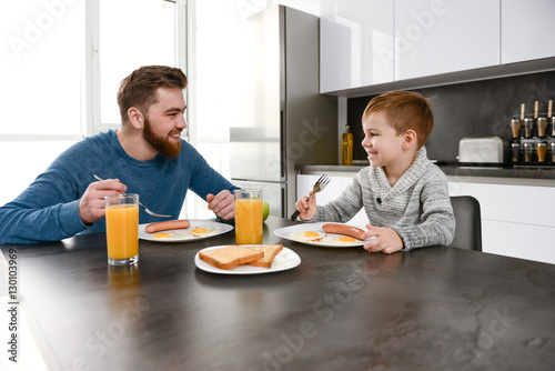 Happy bearded father eating at kitchen with his little son