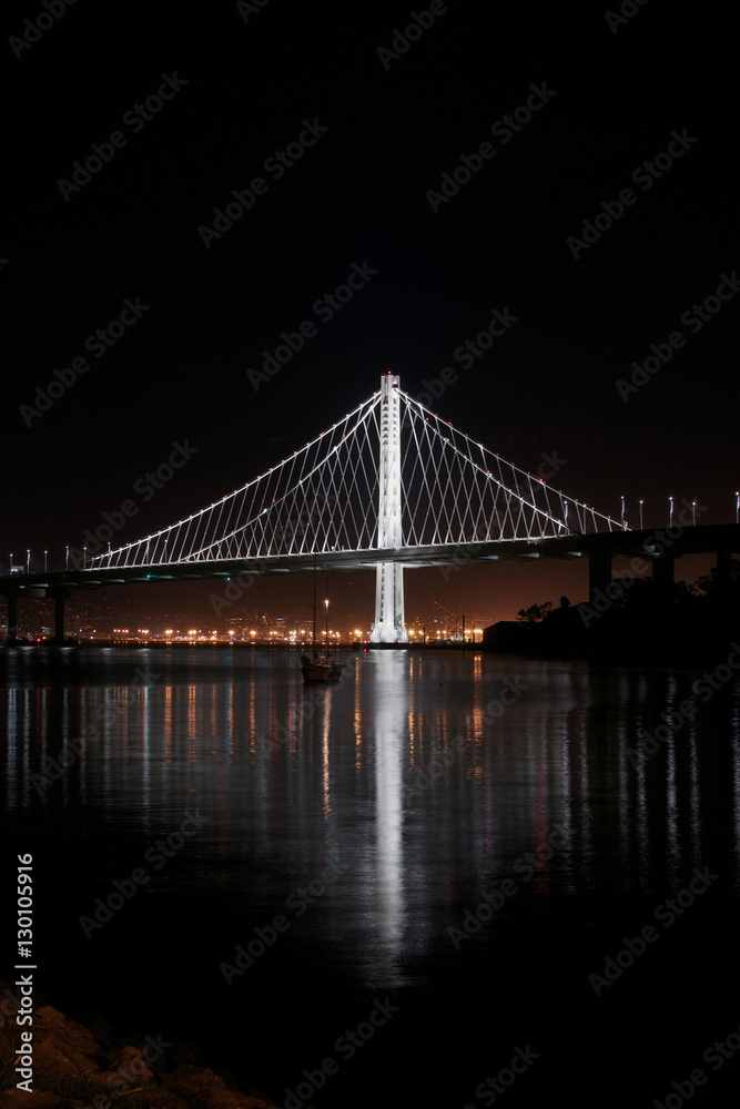 New East Span Bay Bridge illuminated  at night, reflecting glowing lights of the city behind it. Iconic and majestic bridge after dark viewed from Treasure Island in San Francisco.