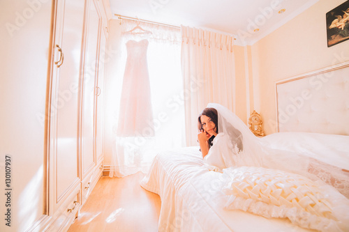 Portrait of beautiful bride. Morning of the bride. Posing on the bed on the wedding morning. Makeup. Brunette girl with long wavy hair. © nataliakabliuk