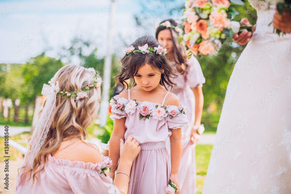 Bride with bridesmaids and little girl kids in the same color dress posing on camera in the park on the wedding day