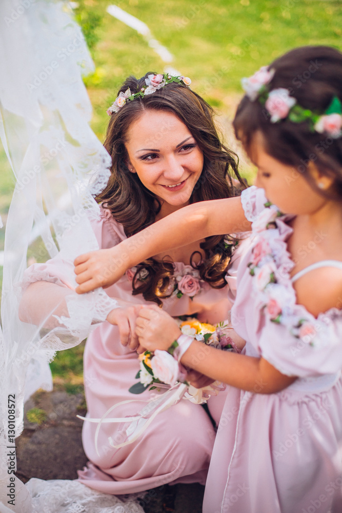 Fototapeta premium Bride with bridesmaids and little girl kids in the same color dress posing on camera in the park on the wedding day