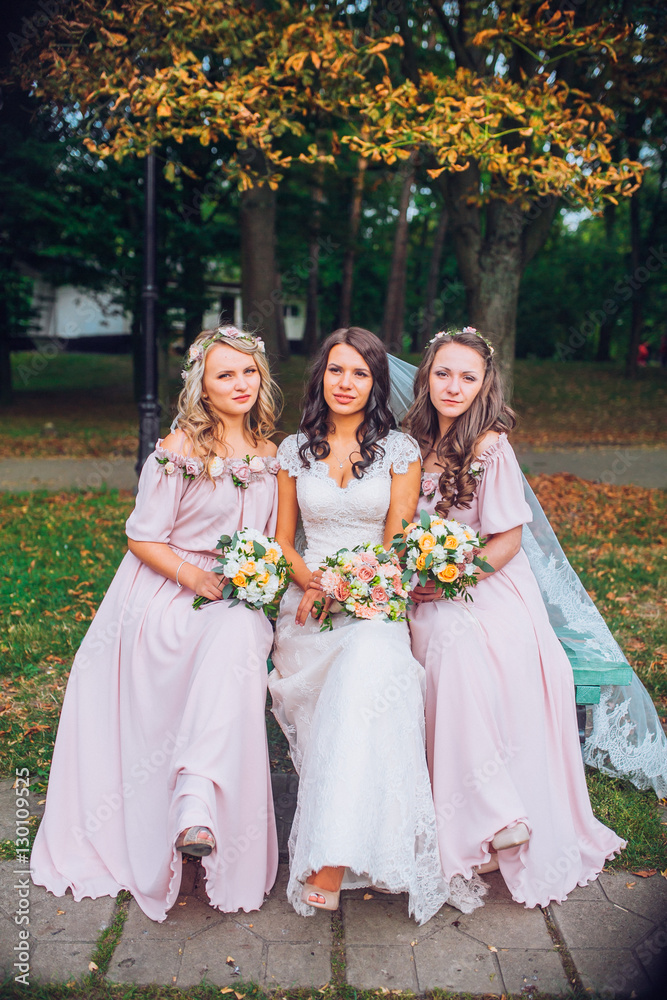 Wedding. The bride in a white dress standing and embracing bridesmaids in green and yellow garden park or forest.