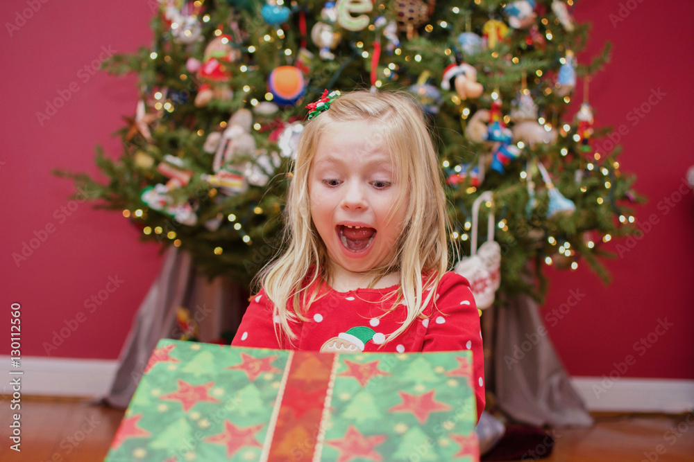adorable school age girl in christmas pajamas opening present under the tree