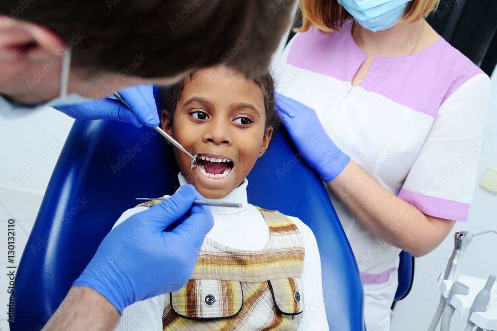 little African-American ethnic black female smiling while dentist in white  latex gloves check condition of her teeth. baby girl in blue dental chair  Stock Photo | Adobe Stock