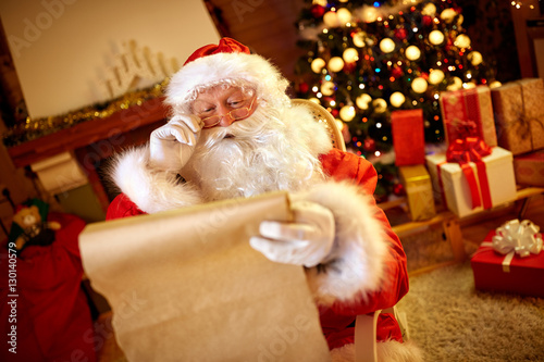 Santa Claus looking at long list with children desire photo