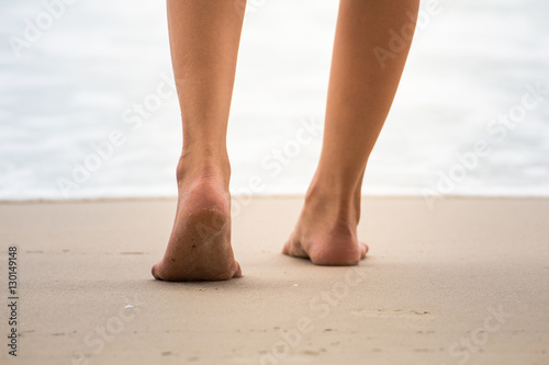 Low angle behind woman walking barefoot on beach