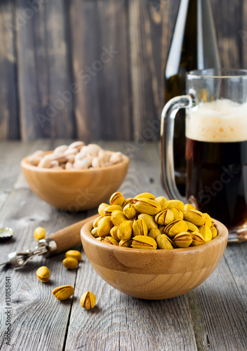 Salted pistachios with saffron and glass of beer on old wooden background. Rustic style. Selective focus.