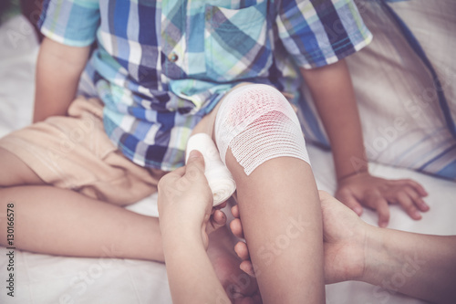 Child injured. Mother bandaging son's knee. Vintage tone effect