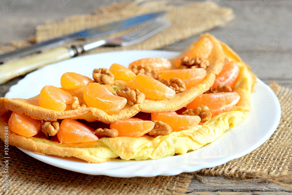 Fruit and nut omelette. Sweet fried omelette stuffed with fresh tangerines and walnuts on a plate. Knife, fork, burlap textile on an old table. Morning breakfast omelette. Healthy lifestyle. Closeup Fruit and nut omelette. Sweet fried omelette stuffed with fresh tangerines and walnuts on a plate. Knife, fork, burlap textile on an old table. Morning breakfast omelette. Healthy lifestyle. Closeup
