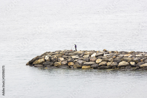 Fisher man with fishing rod on the stone groyne