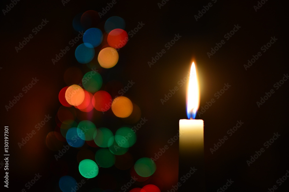 Una candela in primo piano che brilla al buio, accompagnata dalle luci soffuse dell'albero di natale sullo sfondo
