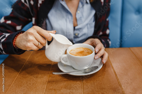 Woman pouring milk in mug of tea from kettle