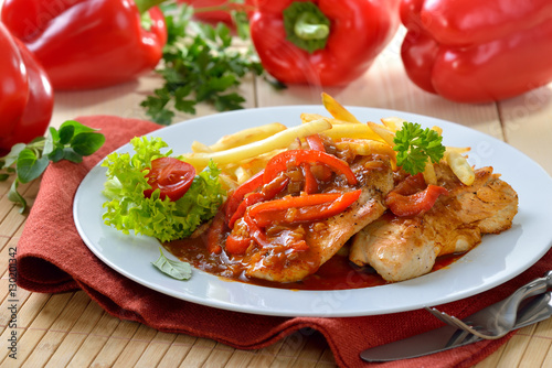 Cuadro en lienzo Deftiges Zigeunerschnitzel mit Pommes Frites vor roten Paprikaschoten - Hot esca