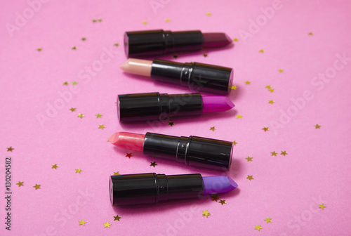 Assorted color lip stick make up on a bright pink background with gold glitter stars
