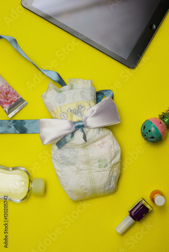 Contents of a woman's bag on yellow background. Contents include: tablet, hand cream, nail polish, baby oil, toy and a diaper.