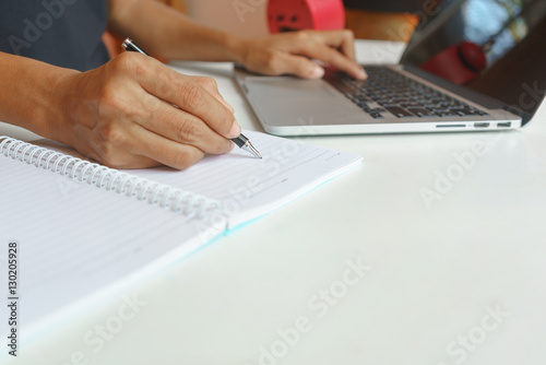 Woman using laptop and writing report on a notebook