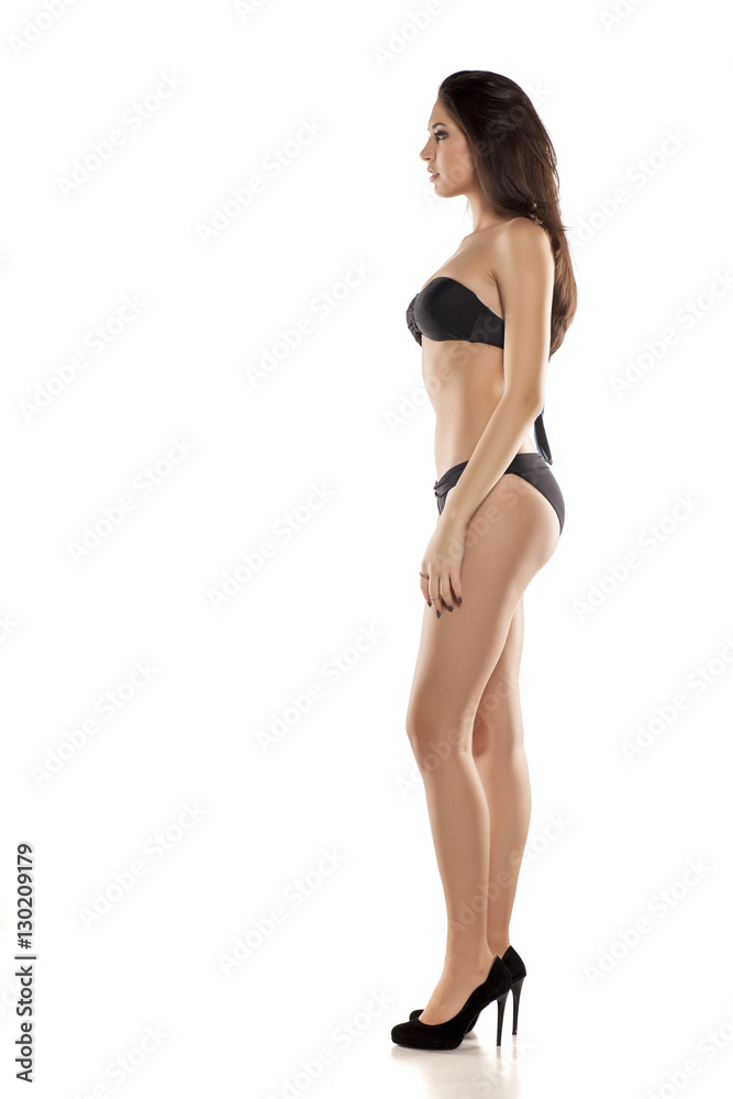 side view of young girl in black bikini posing on a white background