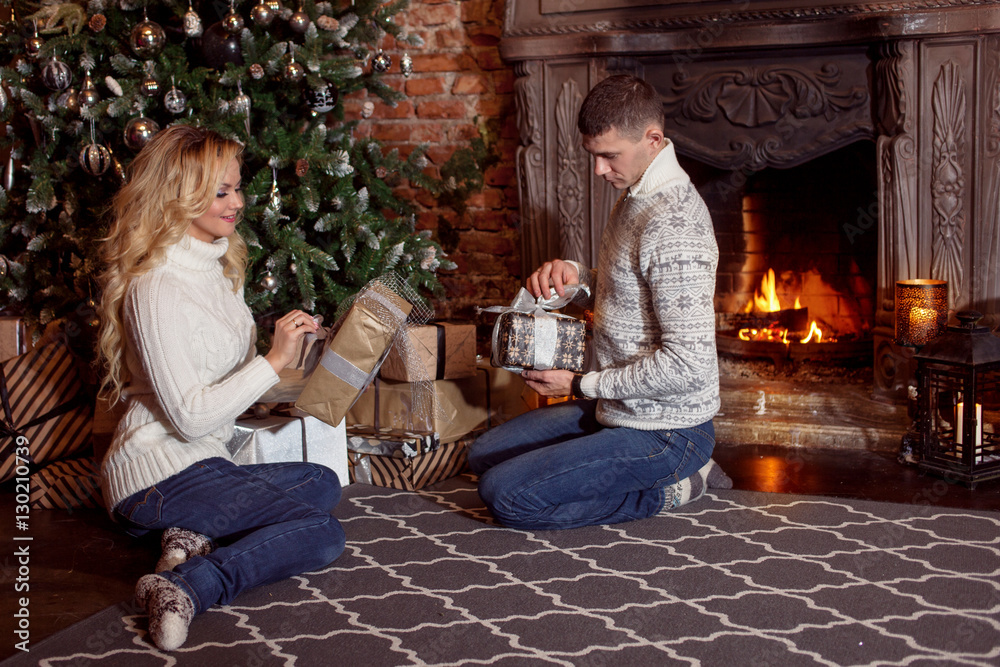 Obraz premium Young couple examines the gifts under Christmas tree. Holiday