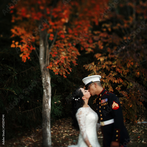 Couple of bride and sailor of US Army kisses under autumn trees