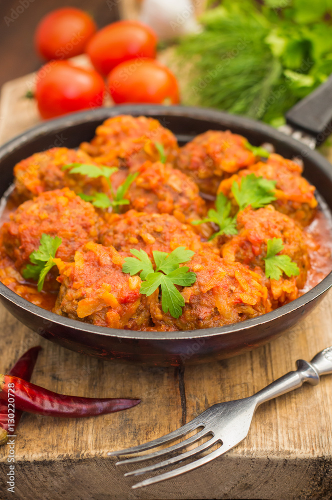 Meatballs in sweet and sour tomato sauce in the pan. Wooden background. Close-up
