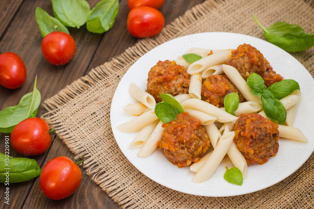 Meatballs with pasta penne in tomato sauce on a white plate. Wooden rustic background. Top view. Close-up