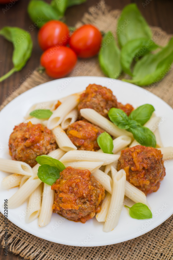 Meatballs with pasta penne in tomato sauce on a white plate. Wooden rustic background. Top view. Close-up Meatballs with pasta penne in tomato sauce on a white plate. Wooden rustic background. Top view. Close-up