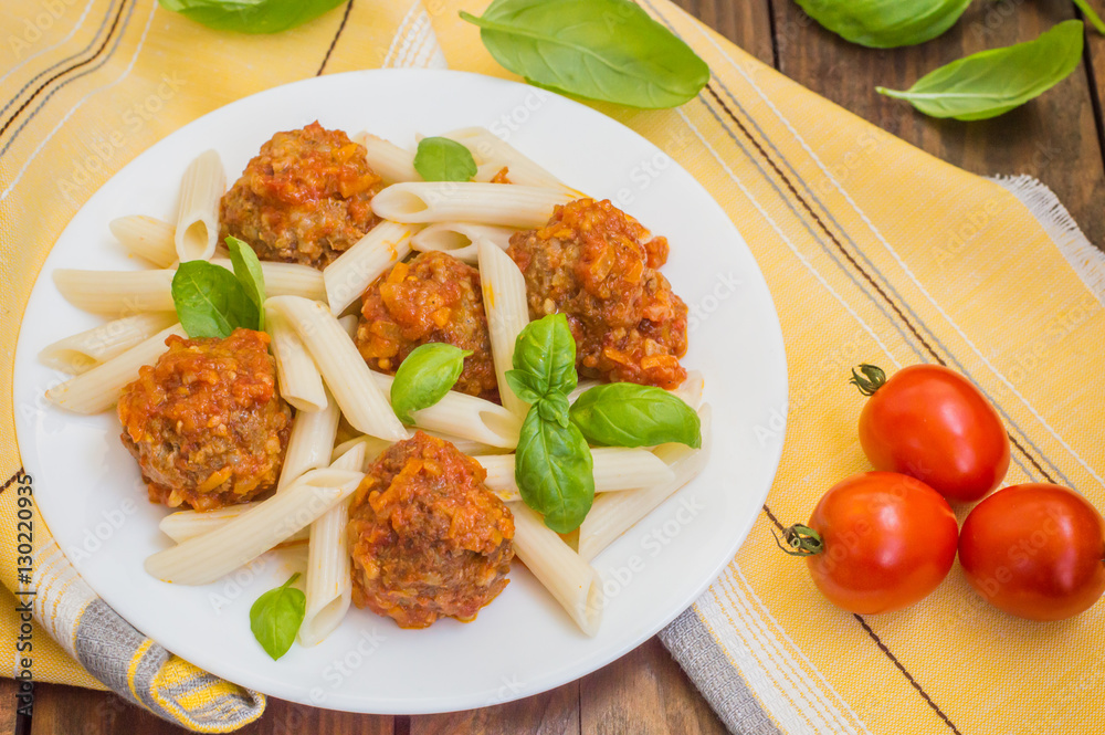 Meatballs with pasta penne in tomato sauce on a white plate. Wooden rustic background. Top view. Close-up Meatballs with pasta penne in tomato sauce on a white plate. Wooden rustic background. Top view. Close-up
