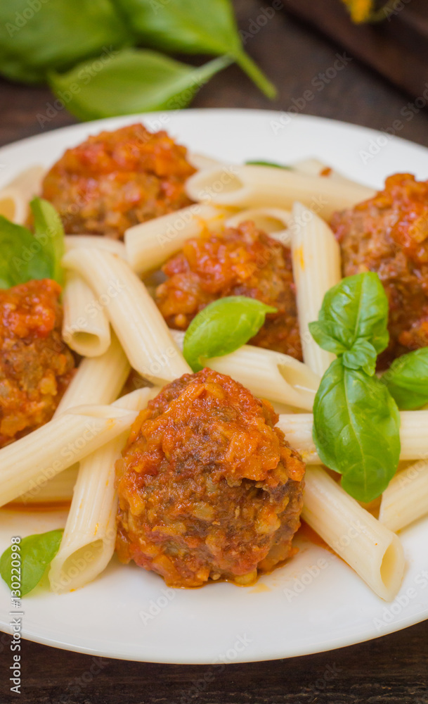 Meatballs with pasta penne in tomato sauce on a white plate. Wooden rustic background. Top view. Close-up Meatballs with pasta penne in tomato sauce on a white plate. Wooden rustic background. Top view. Close-up