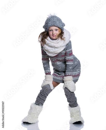 Happy cute kid posing in the studio isolated on white background. Wearing winter clothes. Knitted woolen sweater, scarf, hat, mittens and fashion winter boots with fur.