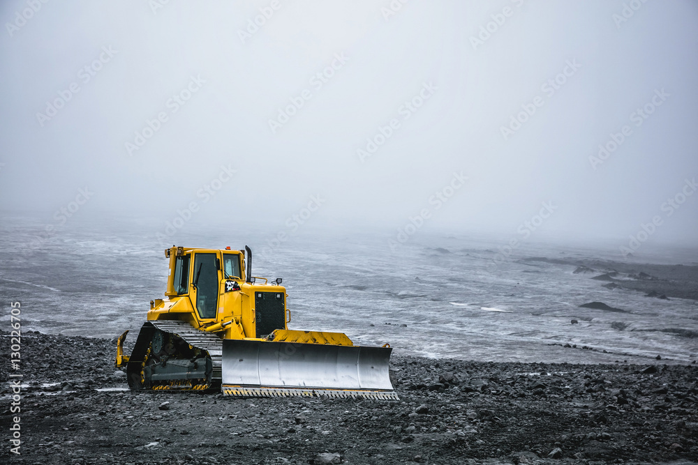 Bright yellow bulldozer on a background of gray desert plateau. Summer in 2016 Iceland