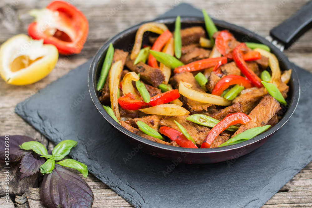 Sauteed beef with vegetables in a pan. Wooden background. Top view. Close-up