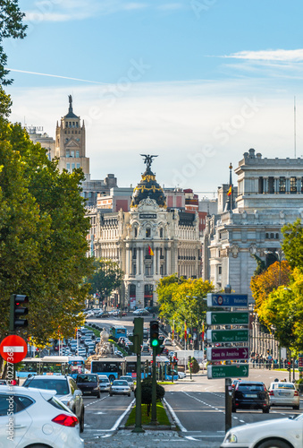 View from Plaza de la Independenci, Madrid, to Metropolis building. Busy, mid-day street scene. Spain urban life, traffic & cars in foreground. 