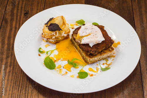 Dish with meat steak on toast, potato chips  melted cheese and poached egg  Dutch sauce. Wooden background. Top view. Close-up