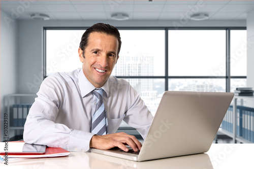  businessman working on computer laptop sitting at desk looking confident