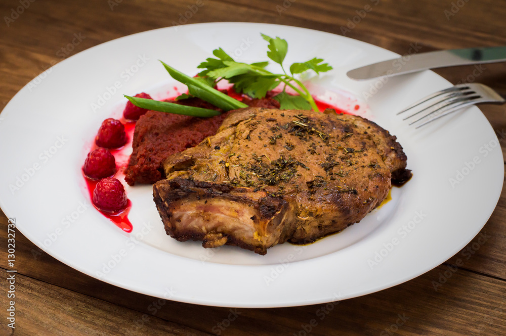 Fried Grilled pork steak on the bone with vegetables, mashed beetroot and berry sauce. Wooden background. Top view. Close-up Fried Grilled pork steak on the bone with vegetables, mashed beetroot and berry sauce. Wooden background. Top view. Close-up