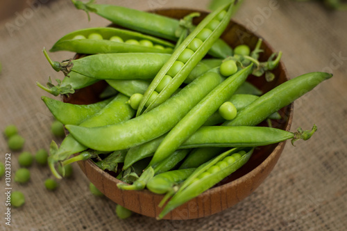 Pea pods in a wooden bowl on sacking.  background. Top view. Close-up