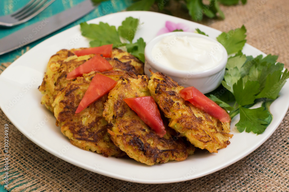 Zucchini Pancakes with sour cream, tomatoes and herbs. Wooden background. Close-up