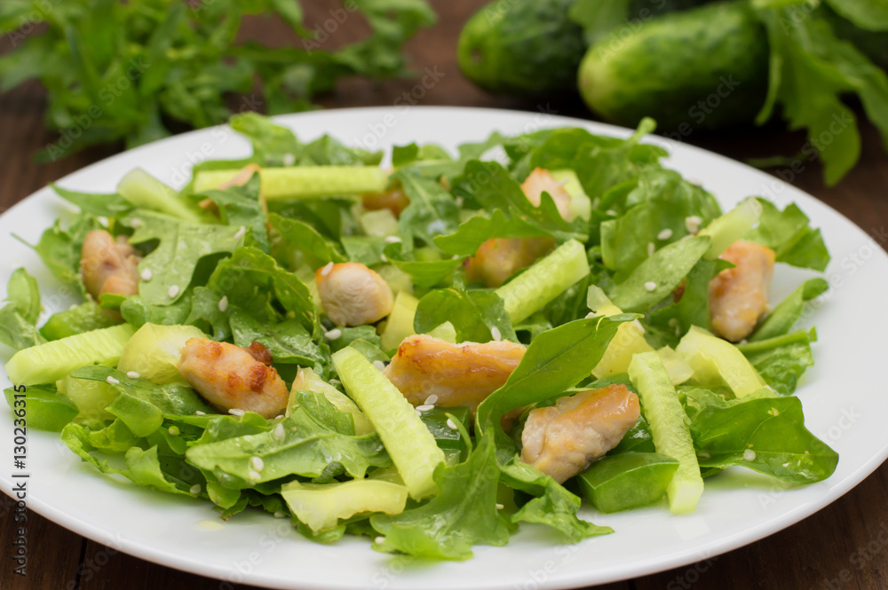 Arugula salad, paprika, cucumber, fried chicken and sesame seeds. Wooden background. Close-up Arugula salad, paprika, cucumber, fried chicken and sesame seeds. Wooden background. Close-up